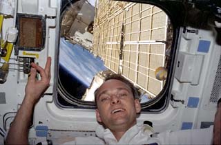 STS-89 Pilot Joe Edwards floats beneath a flight deck window on the Orbiter Endeavour, which frames a solar array on the Mir Space Station. 